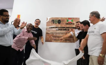 Criciúma inaugura Centro Comunitário no bairro Vera Cruz Autoridades municipais, incluindo o prefeito, vice-prefeito e secretários, sorriem e aplaudem durante a cerimônia de inauguração do Centro Comunitário Vera Cruz. Eles estão descerrando uma placa de tijolos que contém o nome do centro e uma citação.