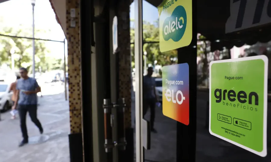 Adesivos de operadoras de vale-alimentação e vale-refeição (Alelo e Green Benefícios) colados na vitrine de um restaurante no Rio de Janeiro, ilustrando o mercado de tíquetes e o novo Decreto do PAT que limita as taxas e visa a interoperabilidade.