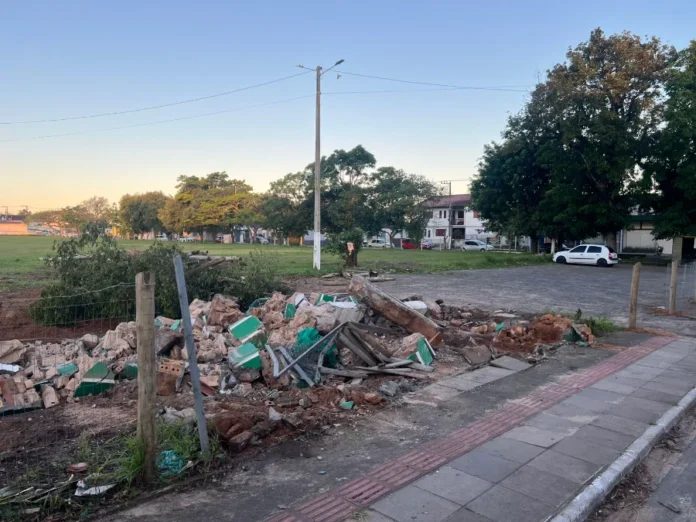 Demolição de portal gera debate sobre história em Sombrio (2) Montanha de escombros do portal demolido no terreno do antigo Estádio Cairú, em Sombrio, com o campo de grama e casas ao fundo, ilustrando a controvérsia sobre o marco histórico da cidade.