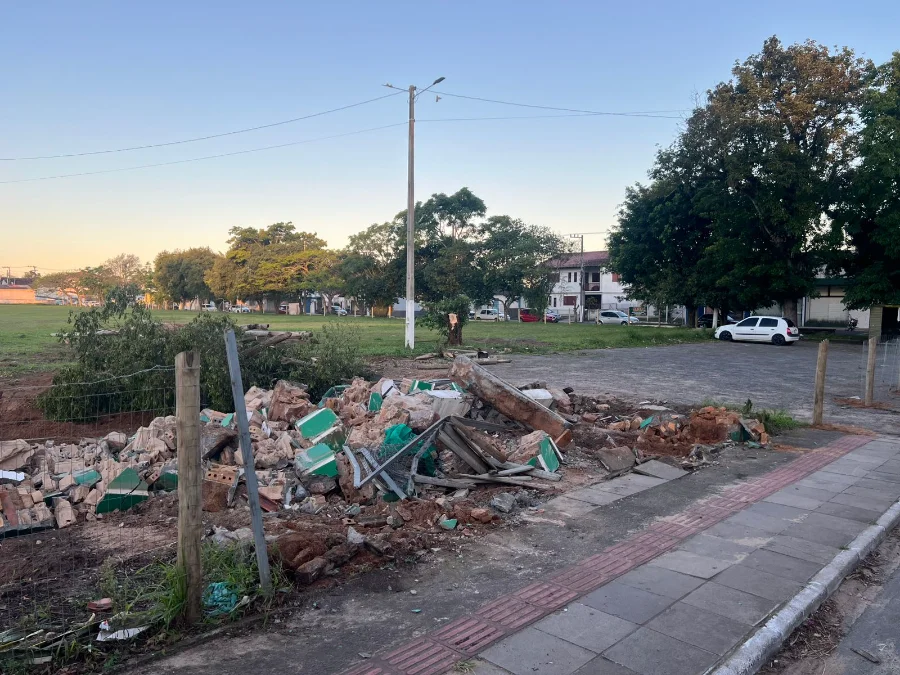 Montanha de escombros do portal demolido no terreno do antigo Estádio Cairú, em Sombrio, com o campo de grama e casas ao fundo, ilustrando a controvérsia sobre o marco histórico da cidade.