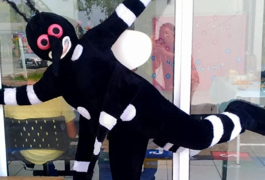 Mascote do mosquito Aedes aegypti, em fantasia preta e branca, participando de atividade lúdica durante o Dia D de Combate à Dengue em frente à ESF Raulino Ramos, em Balneário Gaivota.