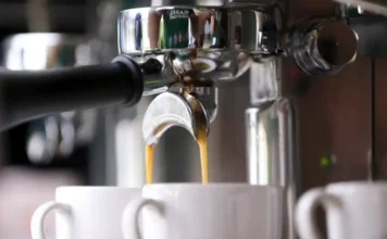 Estudo: Café reduz em 39% risco de arritmia cardíaca Close-up na máquina de café expresso com a bebida sendo extraída em xícaras brancas, ilustrando o consumo diário de café que, segundo estudo de universidades nos EUA e Austrália, reduz em 39% o risco de arritmia cardíaca.