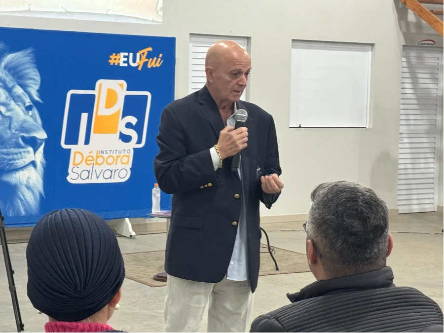 Mentor Jimmy Albuquerque, ex-paciente de câncer, discursando com microfone em um seminário no Instituto Débora Salvaro, compartilhando a experiência de remissão da doença com um método natural focado na limpeza do sangue e no poder da fé.