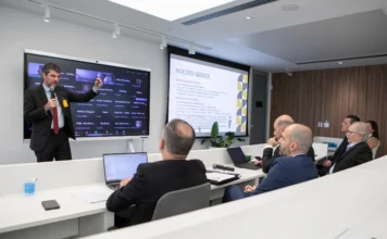 FIESC: Nova lei do IR tem lacunas e gera insegurança jurídica Palestrante de terno aponta para uma tela digital em uma reunião da FIESC, com empresários sentados acompanhando a apresentação sobre a nova lei do Imposto de Renda.