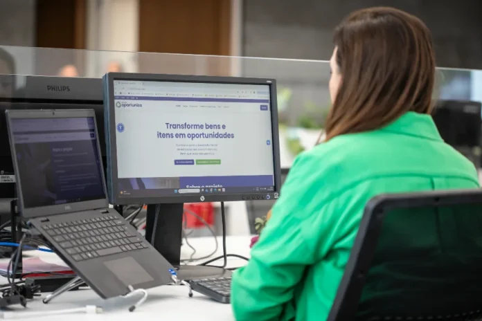 FIESC lança site que conecta indústria e doações Funcionária da FIESC de costas olhando para a tela que exibe o site do Programa Oportuniza da Federação.