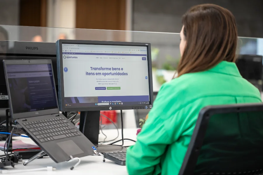 Funcionária da FIESC de costas olhando para a tela que exibe o site do Programa Oportuniza da Federação.
