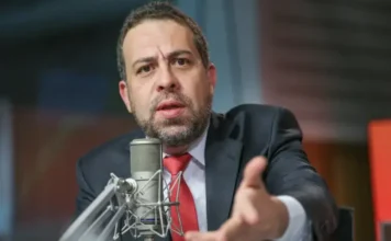 Fim da escala 6×1 deve ter desoneração para microempresas O ministro Guilherme Boulos, de terno e gravata vermelha, em um estúdio, gesticula enquanto fala em um microfone.