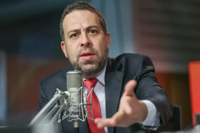 Fim da escala 6x1 deve ter desoneração para microempresas O ministro Guilherme Boulos, de terno e gravata vermelha, em um estúdio, gesticula enquanto fala em um microfone.