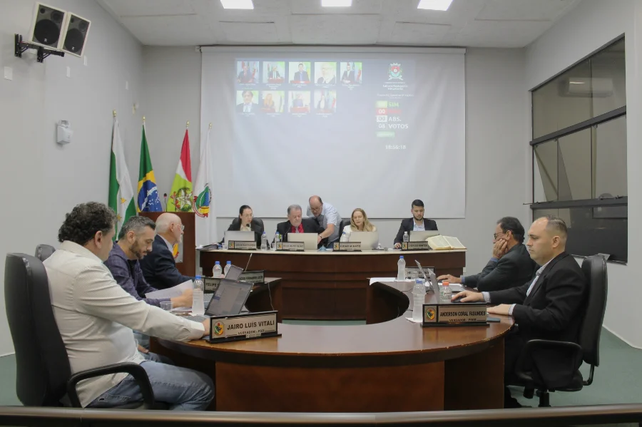 Sessão na Câmara de Vereadores de Forquilhinha com vereadores reunidos à mesa e o telão ao fundo exibindo o placar do novo sistema eletrônico de votação, que visa modernizar os trabalhos do Legislativo.