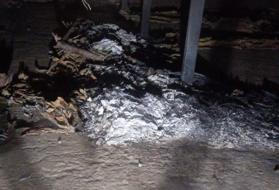 Restos de fumo queimado e cinzas brancas no chão de terra dentro de uma estufa atingida por princípio de incêndio.