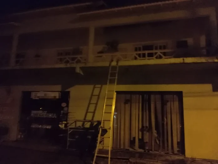 Incêndio atinge prédio em Jacinto Machado Prédio de dois andares atingido por incêndio em Jacinto Machado, com uma escada de bombeiros apoiada na varanda para o acesso ao piso superior.
