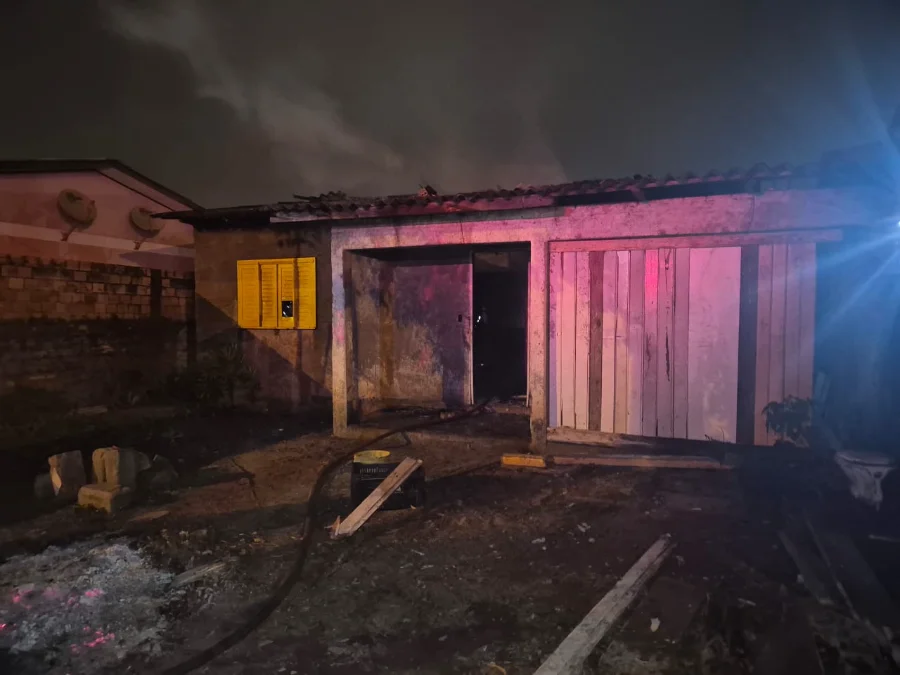 Casa de alvenaria em Araranguá parcialmente destruída por incêndio, com telhado caído e porta de madeira aberta, mostrando os danos causados pelo fogo durante a madrugada.