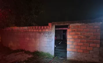 Incêndio de grandes proporções atinge casa em Araranguá Entrada da residência atingida por incêndio em Araranguá, com muro de tijolos e fumaça e luz vermelha (do Corpo de Bombeiros) visíveis no interior da casa.