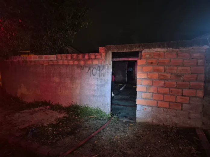 Incêndio de grandes proporções atinge casa em Araranguá Entrada da residência atingida por incêndio em Araranguá, com muro de tijolos e fumaça e luz vermelha (do Corpo de Bombeiros) visíveis no interior da casa.