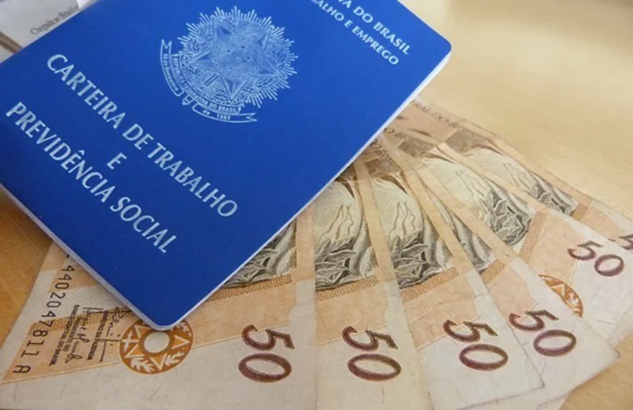 Indústria de SC fecha 2,9 mil vagas, pior resultado desde 2020 Carteira de Trabalho e Previdência Social (CTPS) azul sobre várias notas de R$ 50, simbolizando emprego formal e remuneração.