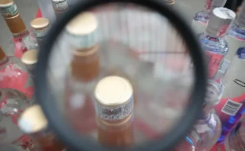 Intoxicação por metanol sobe e soma 16 mortes no país Lupa focaliza o topo de garrafas de bebidas alcoólicas adulteradas, simbolizando investigação de metanol.