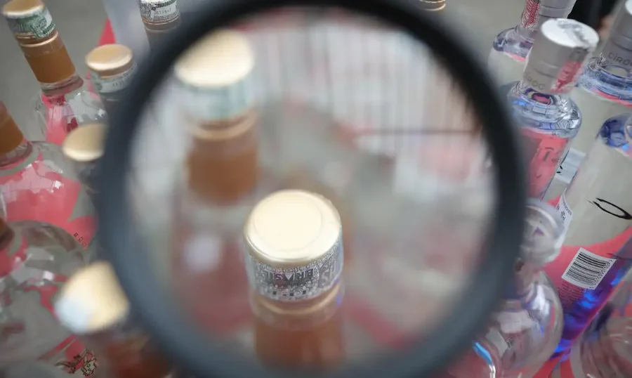 Lupa focaliza o topo de garrafas de bebidas alcoólicas adulteradas, simbolizando investigação de metanol.