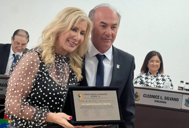 Luciane Ceretta sorri ao receber placa de honraria na Câmara de Turvo, com o vereador Ivonir Arcaro