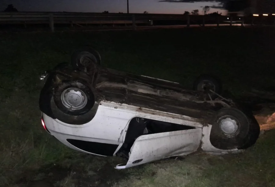 Carro Chevrolet Celta branco capotado, virado de ponta-cabeça na área de grama do vão central da BR-101 em Içara, após acidente noturno que não deixou feridos.