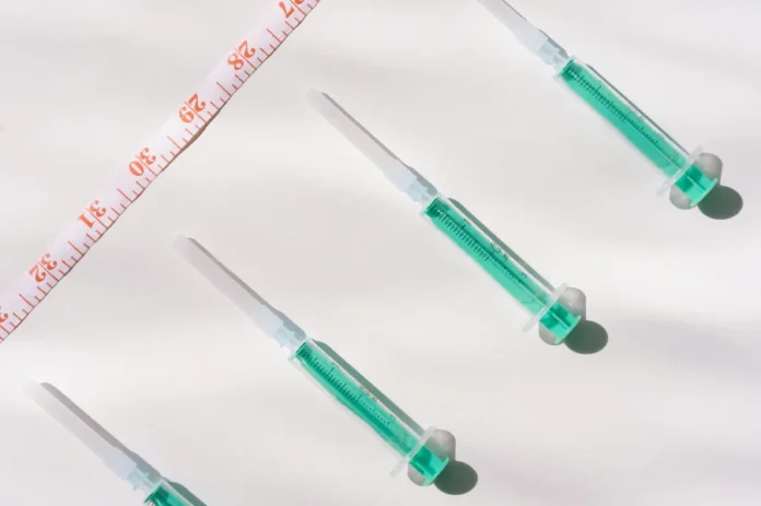 Mounjaro e Nutrição – o que sustenta o resultado! Quatro seringas pré-preenchidas contendo medicamento de cor verde-água (alusão ao Mounjaro/tirzepatida) dispostas diagonalmente ao lado de uma fita métrica.