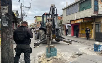 PL mira quem usa barricada para cometer ou ocultar outros crimes Policial de costas observa uma retroescavadeira removendo uma barricada em uma rua estreita de uma comunidade urbana.