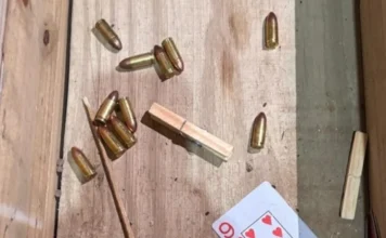 Polícia Civil prende quatro pessoas em operação no Sul de SC Munições de calibre 9mm e .40 espalhadas sobre uma superfície de madeira, ao lado de um prendedor de roupa e uma carta de baralho.