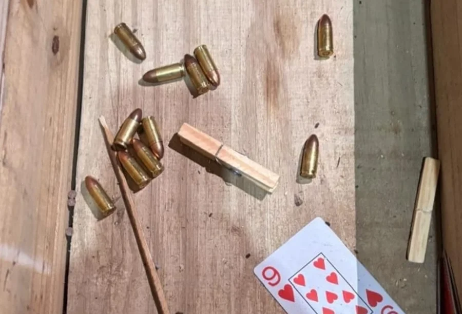 Munições de calibre 9mm e .40 espalhadas sobre uma superfície de madeira, ao lado de um prendedor de roupa e uma carta de baralho.