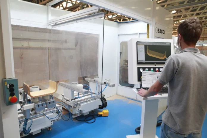 SC tem 2º maior crescimento do país na atividade econômica Operário em uma fábrica controlando uma máquina industrial automatizada que está processando peças de madeira, ilustrando a produção industrial de Santa Catarina.