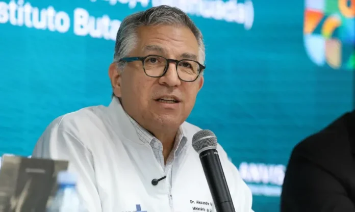 SUS vai ampliar em 30% aproveitamento de plasma O ministro da Saúde, Alexandre Padilha, em um close durante uma coletiva de imprensa, usando óculos e um jaleco médico branco. Ele está falando em um microfone em frente a um fundo turquesa.