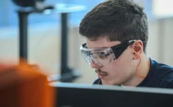 Salário e autonomia são prioridade de jovens no trabalho Jovem trabalhador ou estudante de curso técnico usando óculos de proteção em laboratório ou fábrica, representando a nova geração que prioriza bom salário e autonomia no mercado de trabalho.