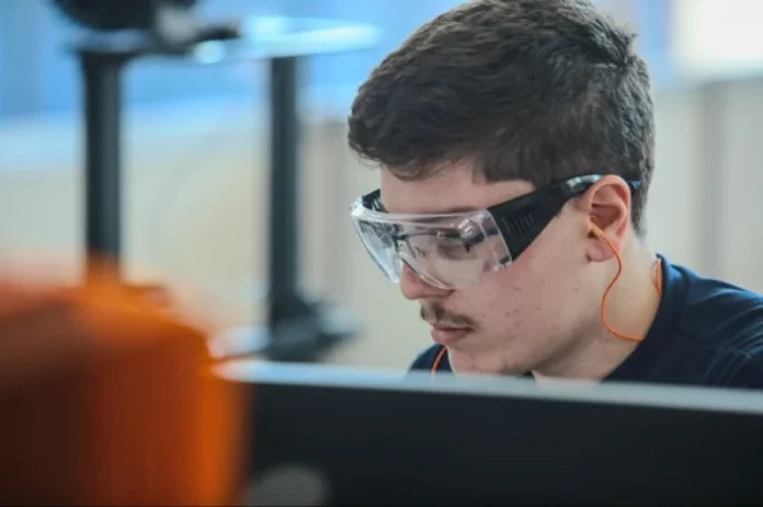 Salário e autonomia são prioridade de jovens no trabalho Jovem trabalhador ou estudante de curso técnico usando óculos de proteção em laboratório ou fábrica, representando a nova geração que prioriza bom salário e autonomia no mercado de trabalho.