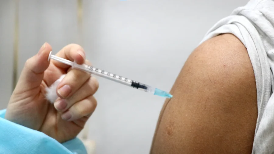 Profissional de saúde aplicando uma vacina no braço de um paciente, com foco na seringa e agulha, simbolizando a prevenção da meningite.