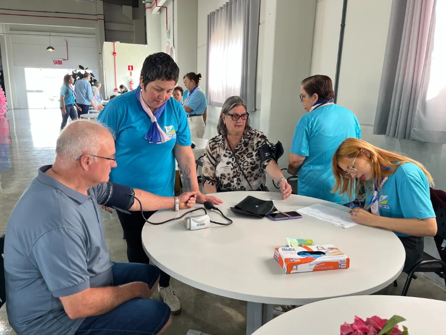 Profissionais de saúde do Balneário Arroio do Silva, vestindo camisetas azuis, aferindo a pressão arterial de um morador durante o evento 