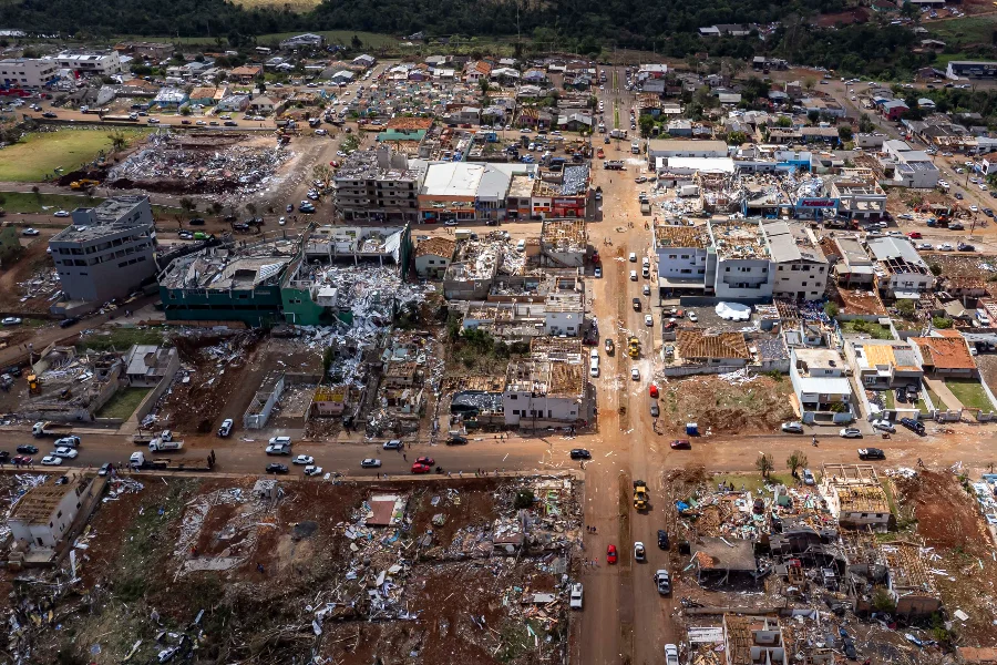 Vista aérea do centro de Rio Bonito do Iguaçu (PR) após ser atingida por um tornado, mostrando casas e edifícios comerciais totalmente destruídos e escombros espalhados pelas ruas, em meio ao apelo urgente por doações para a reconstrução.