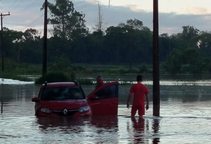 Bombeiro Militar em uniforme vermelho em meio à enchente, auxiliando a retirar um idoso de dentro de um carro submerso em água na Estrada Geral de Itoupava II, em Turvo, após o rio transbordar.
