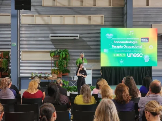 Apresentação em palco de evento universitário, com palestrantes em frente a uma tela que exibe o lançamento dos novos cursos de Fonoaudiologia e Terapia Ocupacional.