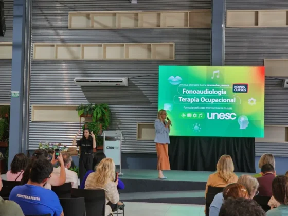 Apresentação em palco de evento universitário, com palestrantes em frente a uma tela que exibe o lançamento dos novos cursos de Fonoaudiologia e Terapia Ocupacional.