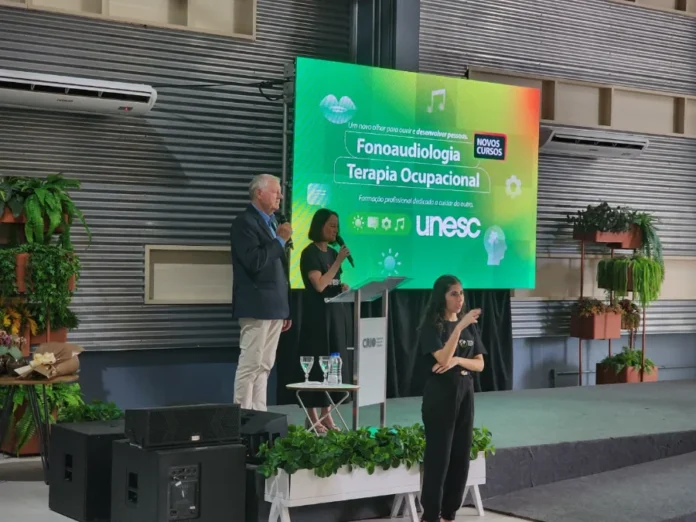 Unesc lança T.O. e Fonoaudiologia para suprir demanda regional (5) Dois palestrantes (um homem e uma mulher) no púlpito, com uma intérprete de Libras à frente, durante o lançamento dos novos cursos da Unesc.