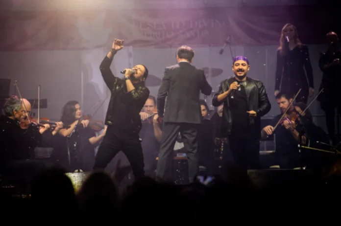 Unesc presenteia Centenário de Criciúma com show da Camerata (1) Músicos da Camerata Florianópolis se apresentam no palco com violino e microfone, sob luzes coloridas durante um show.