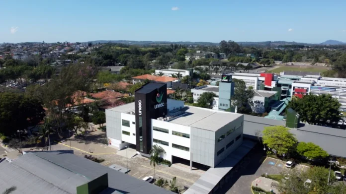 Unesc reafirma papel central no Centenário de Criciúma Vista aérea do moderno campus da UNESC em Criciúma, destacando o prédio principal com o logo vertical, simbolizando o papel da universidade no desenvolvimento da cidade em seu Centenário.