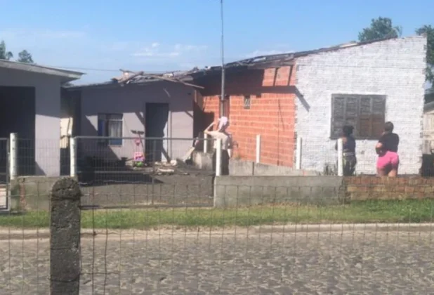 Residência com o telhado parcialmente danificado (destelhamento) no Bairro São Luiz em Sombrio, com moradores observando os estragos do vendaval.