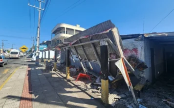 Vendaval causa estragos em Sombrio e Balneário Gaivota Telhado de zinco parcialmente destruído e caído sobre a calçada de uma rua movimentada, ilustrando os danos do vendaval em Sombrio ou Balneário Gaivota.