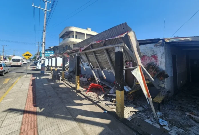 Vendaval causa estragos em Sombrio e Balneário Gaivota Telhado de zinco parcialmente destruído e caído sobre a calçada de uma rua movimentada, ilustrando os danos do vendaval em Sombrio ou Balneário Gaivota.