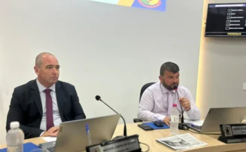 Vereadores de Arroio do Silva pedem reorganização de fiação Dois vereadores sentados em mesa de sessão na Câmara de Balneário Arroio do Silva, com um deles falando ao microfone.