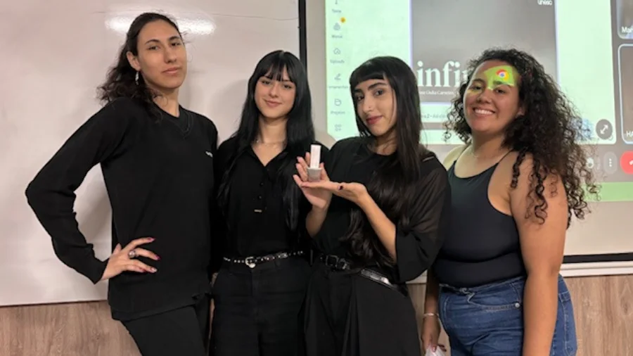 Acadêmicos de Design da Unesc criam projetos para a Dexco Quatro estudantes de Design da Unesc sorriem em frente a um telão de apresentação. Uma das alunas segura um protótipo físico de metal sanitário desenvolvido para a Deca. O grupo veste roupas pretas e azuis, e ao fundo aparece o logotipo do curso e parte da apresentação digital.