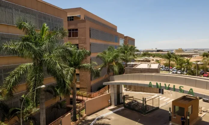 Anvisa manda recolher tônico capilar que simula efeito de Minoxidil Fachada da sede da ANVISA em Brasília, mostrando um prédio marrom de vários andares, palmeiras e a entrada principal com o nome da agência em letras verdes.