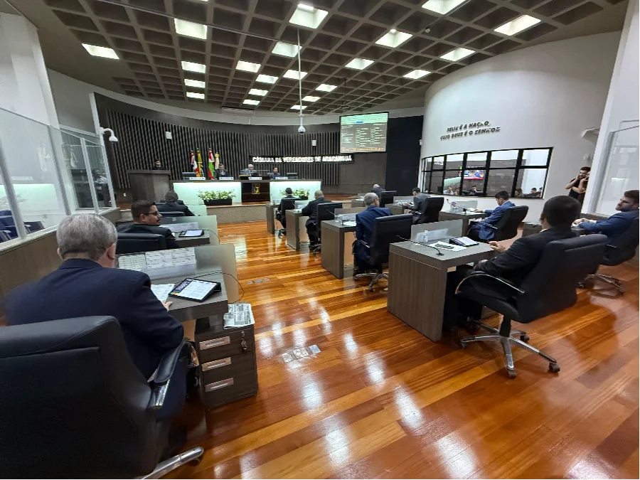 Plenário da Câmara de Vereadores de Araranguá com vereadores sentados em plenário de piso de madeira, durante sessão.