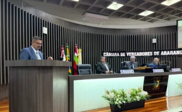 Araranguá aprova lei de assistência à Pessoa com Deficiência O vereador Joel Casagrande discursa no púlpito da Câmara de Vereadores de Araranguá, ladeado por membros da mesa e bandeiras.
