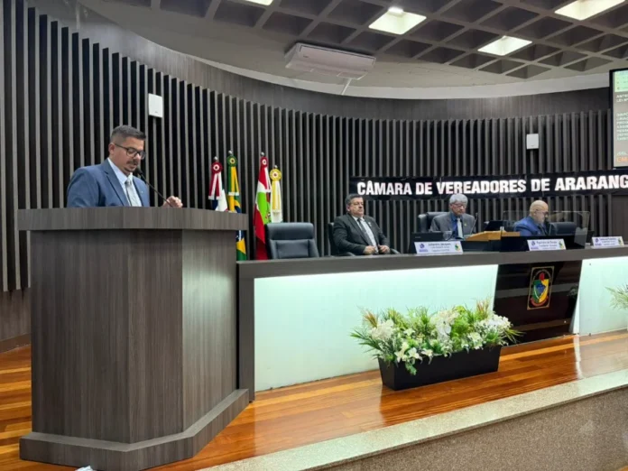 Araranguá aprova lei de assistência à Pessoa com Deficiência O vereador Joel Casagrande discursa no púlpito da Câmara de Vereadores de Araranguá, ladeado por membros da mesa e bandeiras.