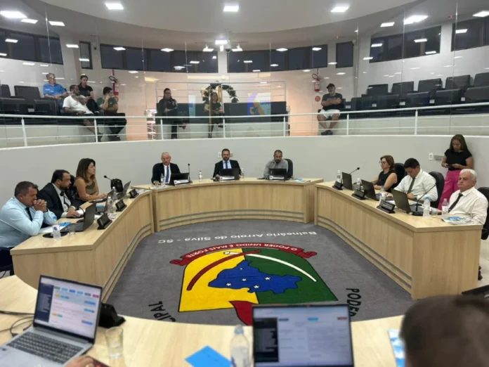 Arroio do Silva aprova orçamento de R$ 99,4 milhões para 2026 Vereadores sentados em plenário semicircular, com o brasão do legislativo no centro do tapete, em Balneário Arroio do Silva.